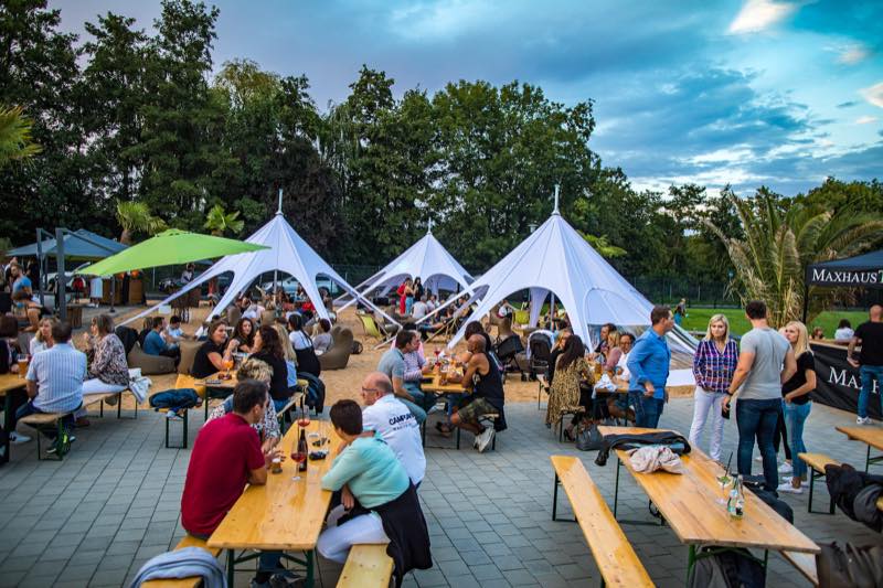 Sommerfest an Biertischgarnituren vor den weißen Sternzelten