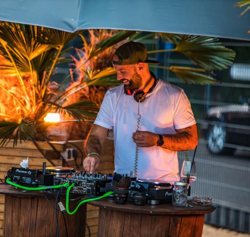 DJ am Pult vor orange angestrahlten Palmen