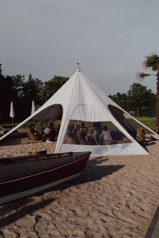 Sternzelt mit Gästen, davor ein Holzboot im Sand