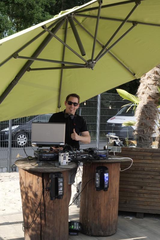 DJ am Pult unter grünem Sonnenschirm