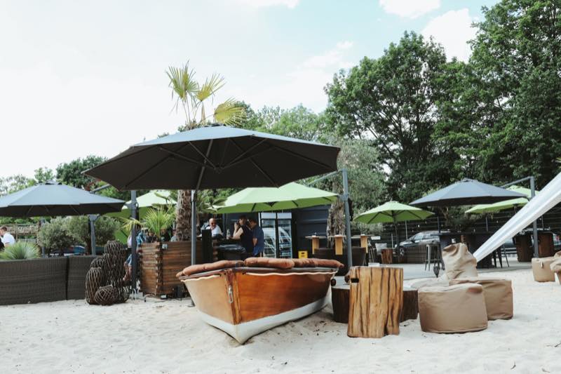 Holzboot und Loungemöbel im Sandbereich unter Sonnenschirmen