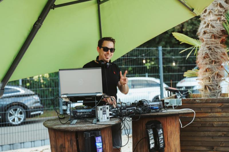 DJ am Pult unter grünem Sonnenschirm