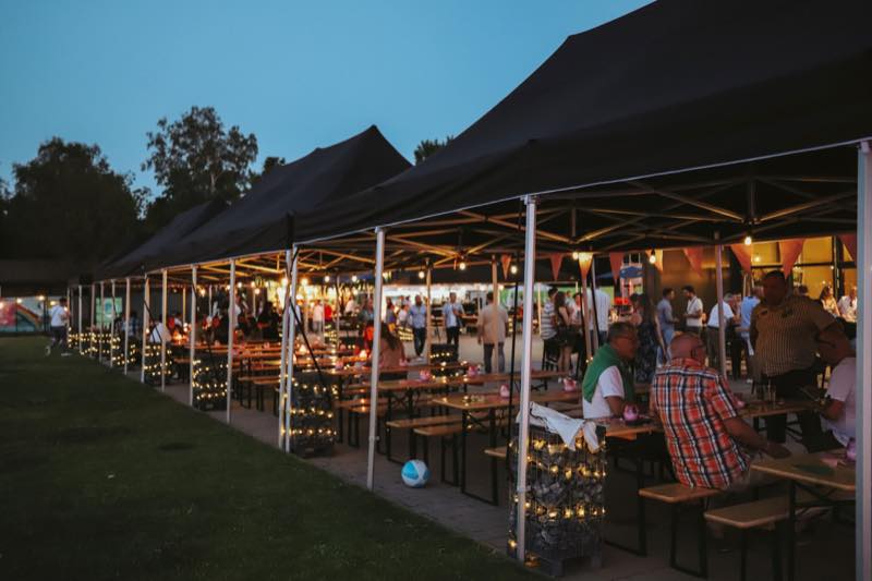Biertischreihen unter Pavillons mit Lichterketten am Abend