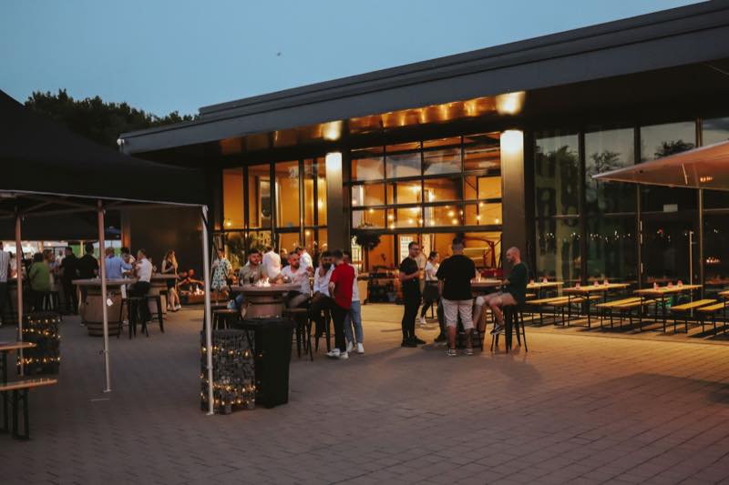 Gäste an Feuertischen vor dem beleuchteten Indoor-Bereich